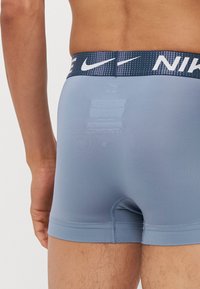 Moške modre atletske kratke hlače s prilagojeno zasnovo. Ponašajo se z vzorčasto temno modro elastiko z logotipom Nike. Gladek, raztegljiv material.