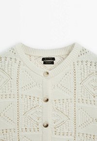 Light cream knitted cardigan with a textured pattern, round neckline, and five button closures. Made of cotton with a breathable design.