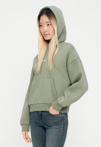 Groene hoodie van een katoenmix, met een voorzak, een trekkoordcapuchon en geribde manchetten. Gecombineerd met donkere denim jeans.