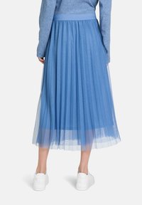Gonna midi a pieghe di colore azzurro chiaro realizzata in tulle trasparente. Presenta una vita elasticizzata e una texture a strati. Indossata con sneaker bianche.