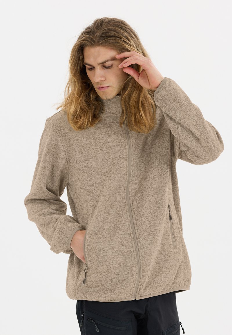 Beige fleecejacka med hög krage, frontdragkedja och två sidofickor. Mjuk textur med ett subtilt mönster och elastiska ärmslut och nederkant.