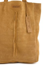 Suede-Shopper aus braunem Material mit strukturierter Oberfläche. Verfügt über dünne Quasten und ein markiertes Lederetikett. Robustes Design mit offenem Oberteil.