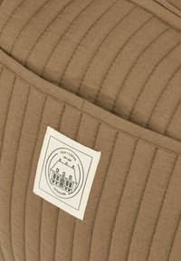 Kockázott barna textil párna függőleges varrással; fehér címkével rendelkezik, amelyen egy ház látható, felirata: "GAI + LIS VA, DÁNIA."