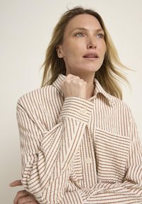 Long-sleeve button-up shirt with a textured, striped pattern in cream and light brown. Features a collar and a single chest pocket.