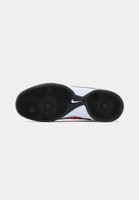 Nike tenisica s potplatom, s crnim gumenim potplatom s teksturiranim uzorkom, bijelim srednjim dijelom i crvenim akcentom.