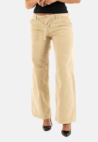 Beige corduroy wijde broek met een knoopsluiting, riemlussen en een gestructureerde afwerking. Gecombineerd met zwarte hoge hakken.