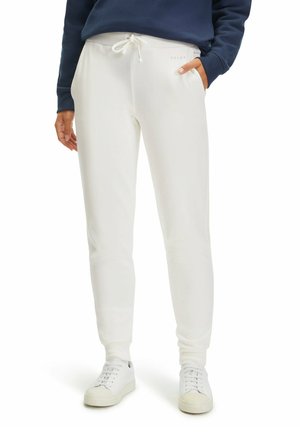 White sweatpants with drawstring waistband, side pockets, fitted cuffs, and textured fabric finish. Paired with white sneakers.
