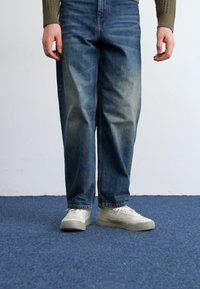 Lyseblå denimjeans med en avslappet passform, litt falmet i midten. Kombinert med beige sneakers med en teksturert såle.