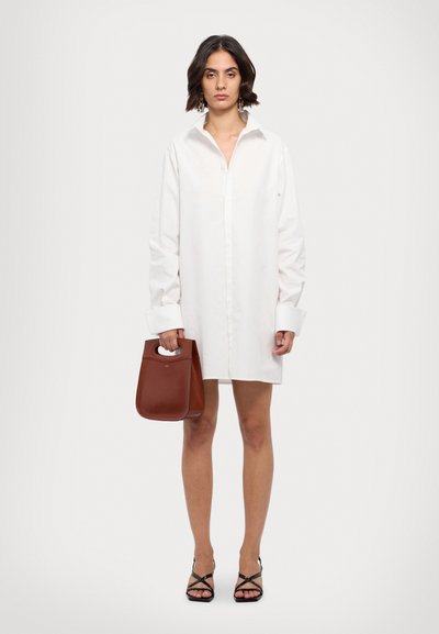 Vit oversized skjortklänning med långa ärmar, knäppning fram och djup krage; tillsammans med en brun läderväska och svarta sandaler med remmar.