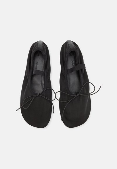 Svarta ballerina-liknande skor av canvas med rund tå, tunna sidenband, elastiska remmar och en slät innerfoder. Inga synliga mönster eller texturer.