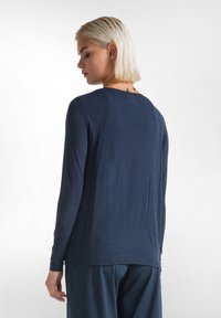 Maglia a manica lunga blu navy in tessuto morbido, presenta un collo rotondo e una vestibilità rilassata, con cuciture minime e un discreto dettaglio di cucitura sul retro.