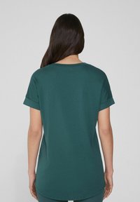 Tyrkysové bavlněné tričko s krátkými ohrnutými rukávy a kulatým výstřihem. Zadní část má rovný střih a jemnou texturu.