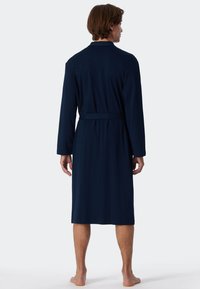 Accappatoio blu navy con maniche lunghe, colletto e cintura. Realizzato in un materiale morbido, presenta una lunghezza fino al polpaccio e un design minimal.