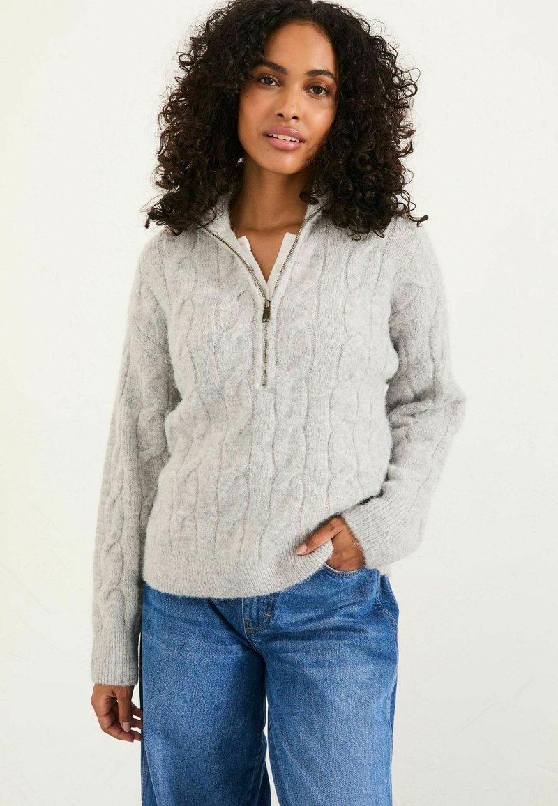 Hellegrau gestrickter Pullover mit Reißverschluss-Kragen, langen Ärmeln und weicher Textur. Kombiniert mit lockeren blauen Denim-Jeans.