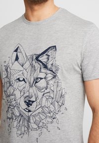 Camiseta de algodón gris con un diseño geométrico de un lobo en azul marino, con formas angulares y detalles similares a cristales que rodean la cara del lobo.