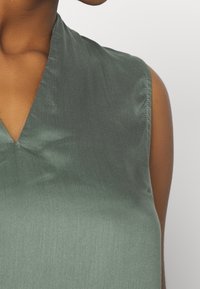 Satinoberteil in gedecktem Grün mit einem tiefen V-Ausschnitt und ärmellosem Design. Glatte Textur mit subtiler Schimmerung und sauberen Nähdetails.