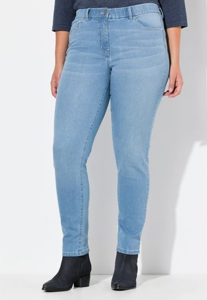 Hellblaue Jeans aus Denim mit dezentem Schimmer, mittelhoher Taille, kombiniert mit schwarzen Stiefeletten und einem dunklen Langarmshirt, dargestellt von der Taille bis zu den Füßen.