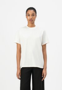 White cotton t-shirt with a round neck and short sleeves, featuring an embossed logo on the left chest. Smooth texture, relaxed fit.
