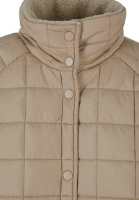 Beige pūkains džemperis ar augstu apkakli, quilted rakstu un snap pogām. Iekšpuse ir ieklāta ar mīkstu, teksturētu audumu.