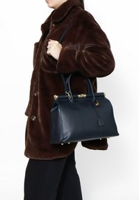 Marine leren handtas met een gestructureerde vorm, bovenhandvatten, goudkleurige hardware en een gladde textuur. Tentoongesteld tegen een witte achtergrond.