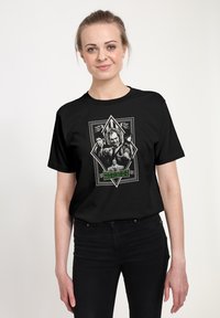 Czarny bawełniany t-shirt z graficznym nadrukiem postaci z "Beetlejuice" w diamentowej ramce, z zielonymi i szarymi detalami.