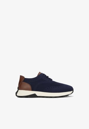 Baskets en maille bleu marine avec détail en cuir marron au talon, semelle intermédiaire blanche, semelle extérieure noire et avant à lacets, présentées de profil.