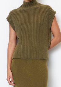 Olivengrøn strikket sweater med høj krave, korte ærmer, ribbet tekstur og en løs pasform. Parret med en matchende nederdel.