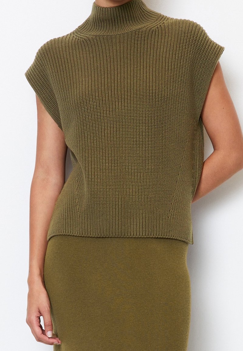 Olivengrøn strikket sweater med høj krave, korte ærmer, ribbet tekstur og en løs pasform. Parret med en matchende nederdel.