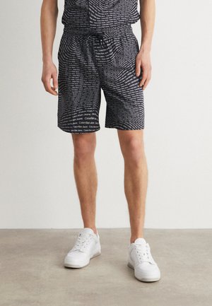 Pantalones cortos negros con un patrón de texto repetido que dice "Calvin Klein Jeans", fabricados en un tejido ligero, con cintura elástica y cordón ajustable.