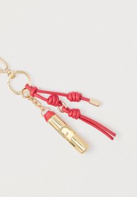 Μπρελόκ με χρυσά μεταλλικά στοιχεία, κόκκινες δερμάτινες λεπτομέρειες και κυλινδρικό γούρι με λογότυπο. Περιλαμβάνει κόμπους από δέρμα.