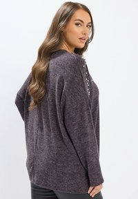 Maglione oversized viola con una texture morbida, con un colletto e bottoni decorativi lungo il davanti. Il design offre una vestibilità rilassata.
