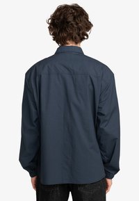 Navyblauwe langemouwen shirt van lichtgewicht stof. Heeft een kraag, een rugpand en elastische manchetten.