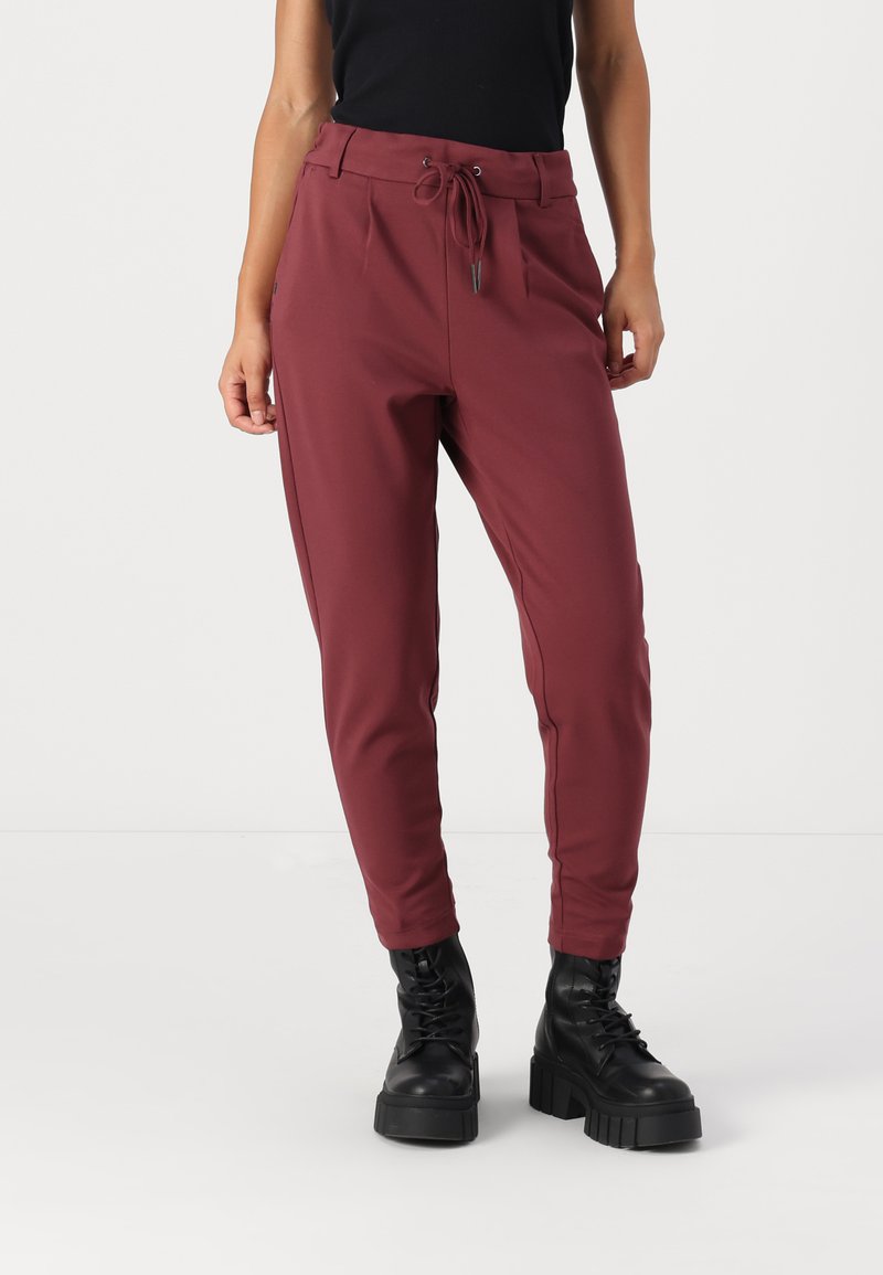 Pantaloni jogger bordeaux con vita regolabile, tasche laterali e vestibilità affusolata, abbinati a stivali neri con suola spessa e lacci. Tessuto dalla consistenza liscia.