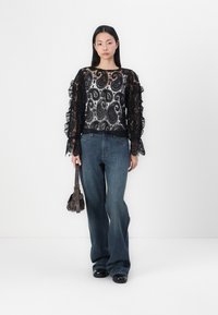 Schwarzes Spitzenshirt mit langen Ärmeln und Rüschensaum, mit einem Paisleymuster, kombiniert mit blauen weit geschnittenen Jeans und einer kleinen braunen Handtasche.