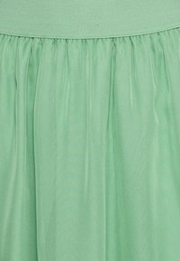 Jupe en tissu vert menthe avec une large ceinture texturée, dotée de douces plis sur toute sa longueur pour une silhouette fluide.