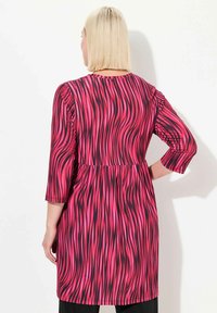 Fuksia mekko mustilla aaltoilevilla kuvioilla, kolmannes hihoilla ja kerätyllä vyötäröllä. Silkkinen kangas rentoa istuvuutta, ulottuen reiden puoliväliin.