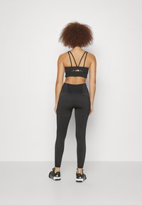 Black sports bra with multiple crisscross straps and high-waisted leggings featuring contrasting gray vertical stripes. Black athletic shoes.