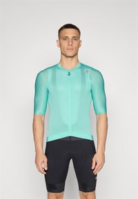 Kurzarm-Radtrikot in hellem Türkis, aus Mesh-Stoff, mit einem Reißverschluss vorne und tailliertem Schnitt. Getragen mit schwarzen Radshorts.