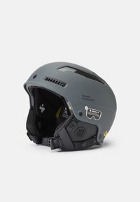 Casco de esquí gris con ranuras de ventilaci�ón, diseño robusto, interior acolchado y correas ajustables. Presenta logotipos y adhesivos de certificación de seguridad.
