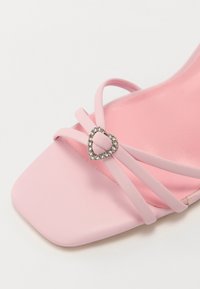 Rozā augstpapēžu čības ar kvadrātveida purngalu, ar delikātiem siksniņām un sirds formas rhinestone akcentu priekšpusē. Gluda tekstūra.