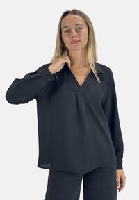 Blusa nera con maniche lunghe, scollatura a V, dettagli a pieghe sul davanti e polsini con bottoni. Il tessuto appare liscio e leggero.