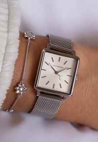 Quadratische silberne Uhr mit Mesh-Armband, einem cremefarbenen strukturierten Zifferblatt und silbernen Stundenmarkierungen. Verfügt über ein zartes silbernes Armband mit floralen Akzenten.