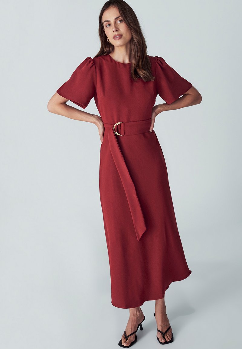 Robe midi rouge avec de courtes manches bouffantes, une ceinture à la taille avec une boucle en or et une silhouette droite ; tissu doux et texture lisse.