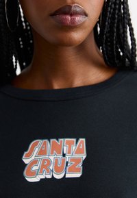 Svart kortermet t-skjorte med teksten "SANTA CRUZ" i livlige orange og blå grafisk design, glatt stoff, rund hals.