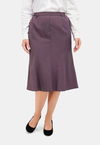 Lila Rock mit ausgestelltem Design, strukturiertem Stoff, einem elastischen Bund mit Ringdetails und knielangem Saum. Dazu werden schwarze Ballerinas getragen.