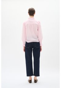 Rosa bluse med puffede ærmer, flæsekrave og samlet ryg, parret med mørkeblå vidde jeans og dyreprint sko.