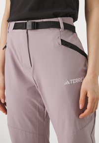 Light purple outdoor pants with black accents. Features include a black belt, side zippers, and a white "TERREX" logo on the thigh.