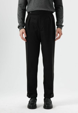 Black pleated trousers with a tailored fit, featuring a button closure, rolled cuffs, and a smooth texture. Paired with black loafers.