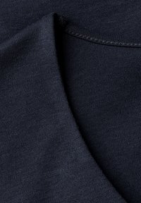 Mörkblå bomullstyg med en slät textur, som har en vikt kant och en sömdetalj längs halsringningen. Närbild.