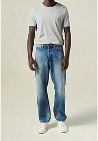 Camiseta gris claro combinada con jeans azules desgastados. Los jeans tienen un corte recto, una cintura de altura media y un diseño típico de cinco bolsillos. Zapatillas blancas.